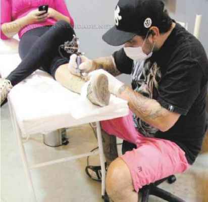 Com luvas e máscara, Marcelo Raposo atende uma cliente em sue estúdios de tatuagem