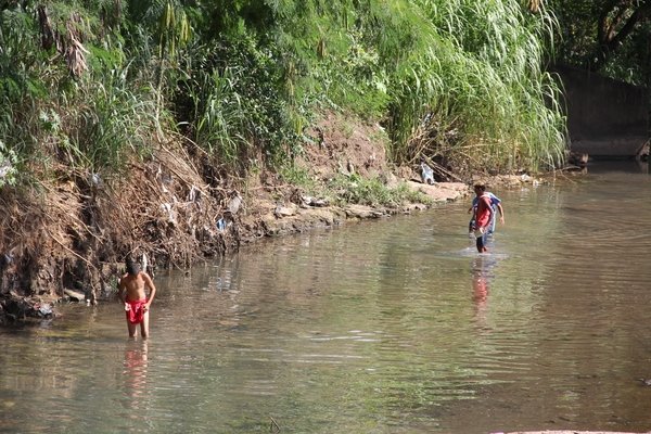 Jovens passam pelo Córrego da Servidão, em trecho localizado na Avenida Visconde do Rio Claro